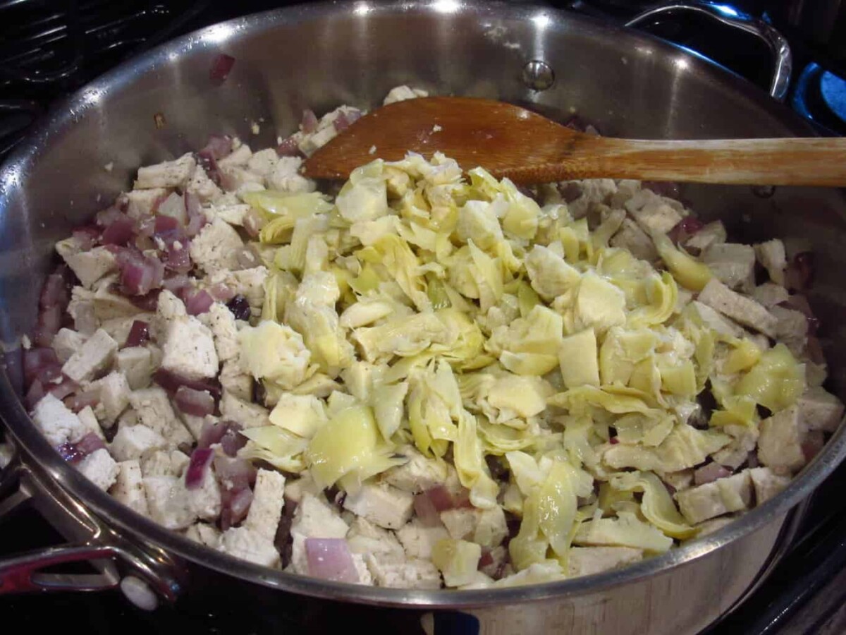 Chopped artichokes in a pan of chicken and onions.
