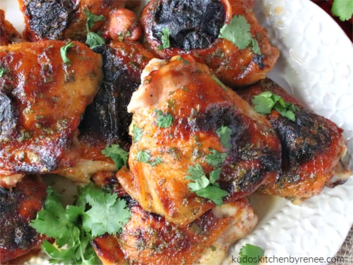 An extreme closeup horizontal photo of an easy dinner recipe for honey lime sriracha chicken thighs with chopped cilantro garnish.
 