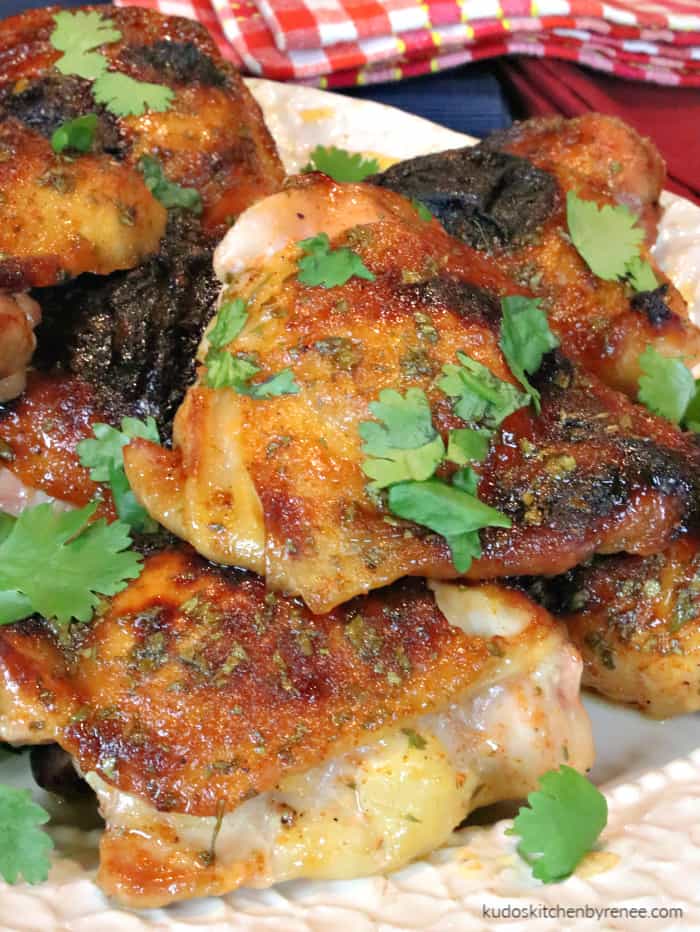 A vertical closeup image of golden brown and succulent chicken thighs with honey lime sriracha sauce piled on a plate with fresh cilantro.