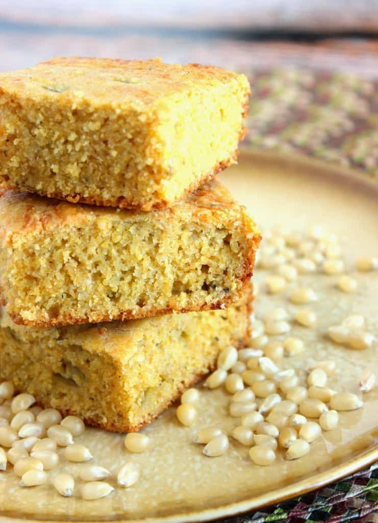 A vertical photo of an offset stack of cornbread squares with corn kernels on the plate.