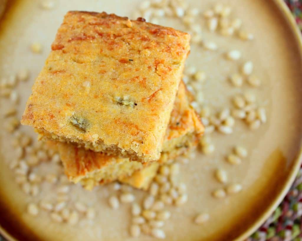 A horizontal overhead photo of a stack of Jalapeno cheddar cornbread on a golden color plate with corn kernels on the plate.