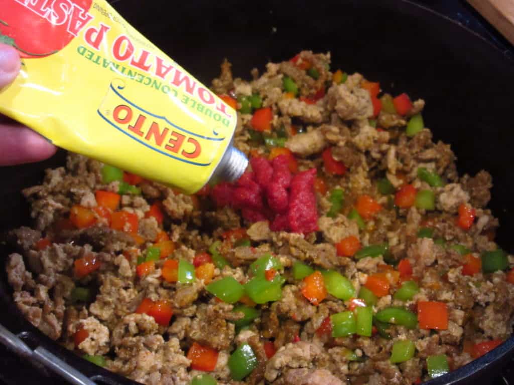 Tomato paste being squirted into a pot of browned turkey.