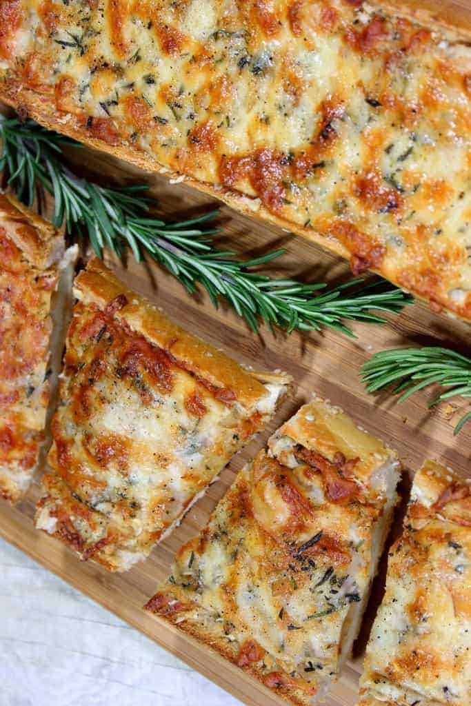 A closeup vertical overhead photo of garlic cheese bread with rosemary sprigs. A BBQ side dish for pulled pork, or chicken.