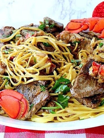 A big plate of Steak and Lobster Linguine with a red and white tablecloth.