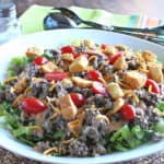 A huge big mac salad in a white bowl with tongs in the background.