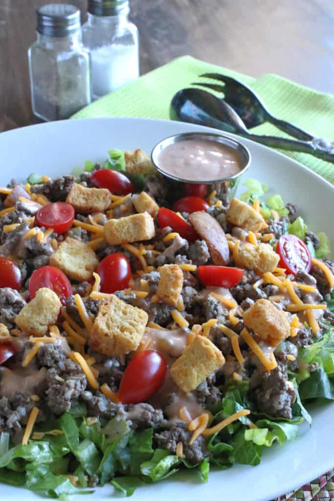 A closeup vertical image of a main course salad big mac salad with ground beef, tomatoes, romaine lettuce and special sauce in a cup.