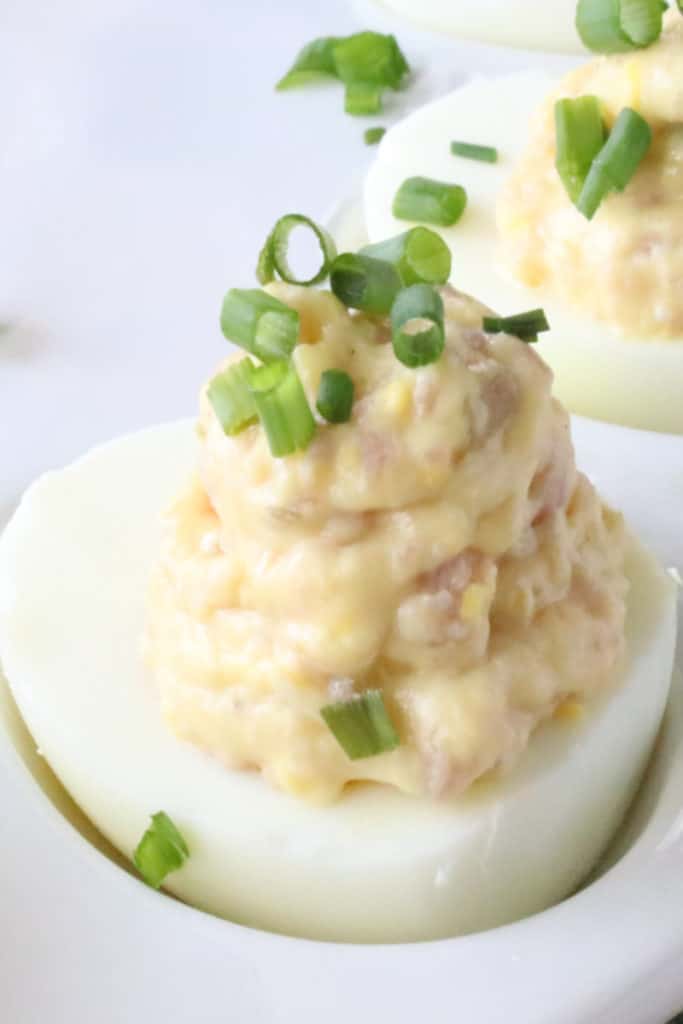 Extreme vertical closeup photo of a stuffed hard-boiled egg with ham and chives. Deviled Dijon Ham and Eggs