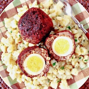 Two perfectly cooked Scotch Eggs on a plaid plate with potatoes.