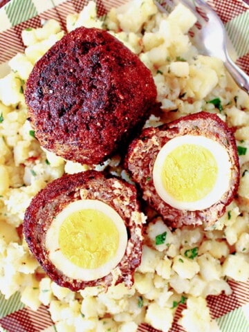 Two perfectly cooked Scotch Eggs on a plaid plate with potatoes.