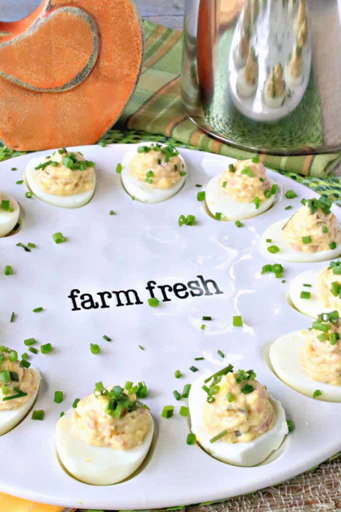 A vertical closeup image of deviled eggs on a white farm fresh plate with chopped chives as garnish. Deviled Dijon Ham and Eggs