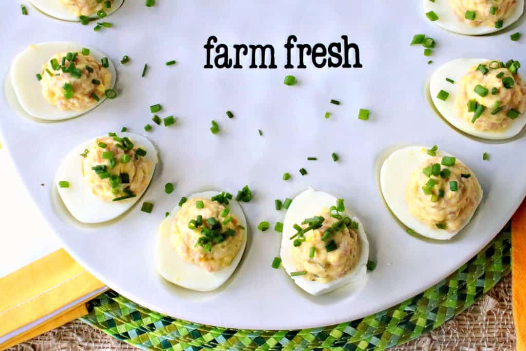 An overhead horizontal photo of a platter of deviled Dijon eggs with ham and chives as garnish on a green place mat with yellow accents.