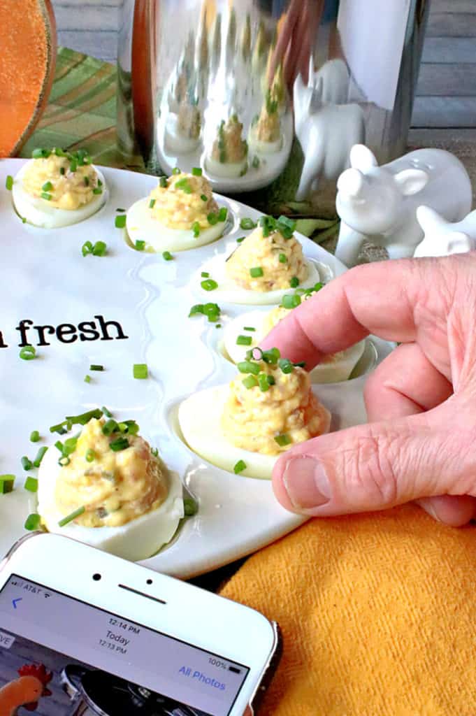 A vertical closeup photo of a hand reaching for a deviled Dijon ham and egg off an egg platter.