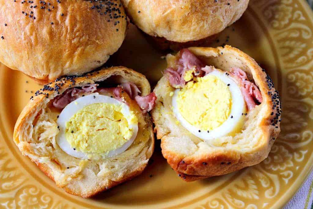 An overhead horizontal photo of a hard boiled egg stuffed biscuit with ham and cheese that is cut in half on a yellow plate.