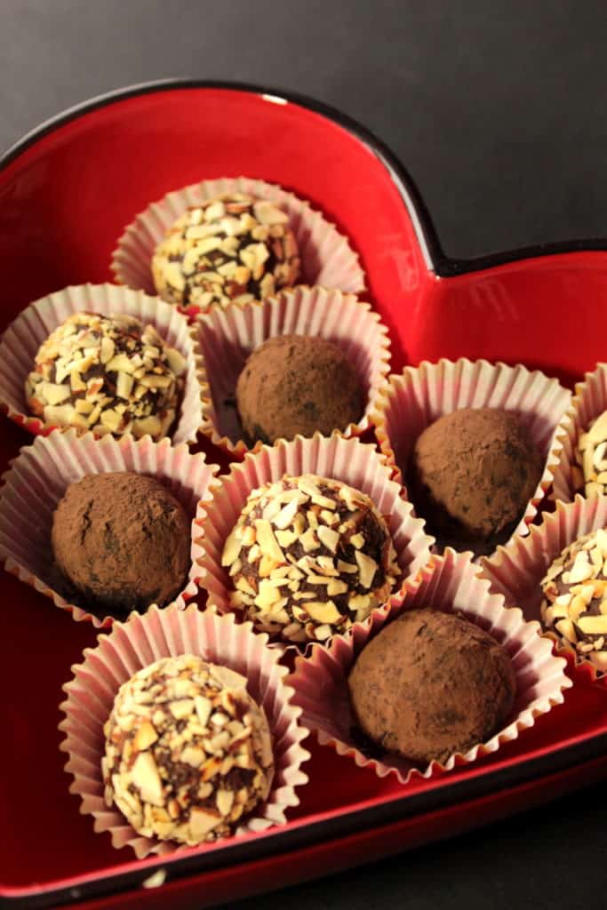 A vertical closeup image of a bunch of homemade chocolate valentine candy in a red heart shaped dish. Mexican chocolate truffles.