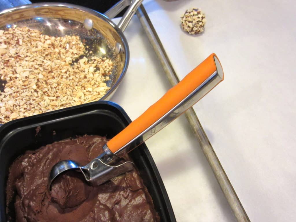 A small cookie scoop in a container of chocolate.