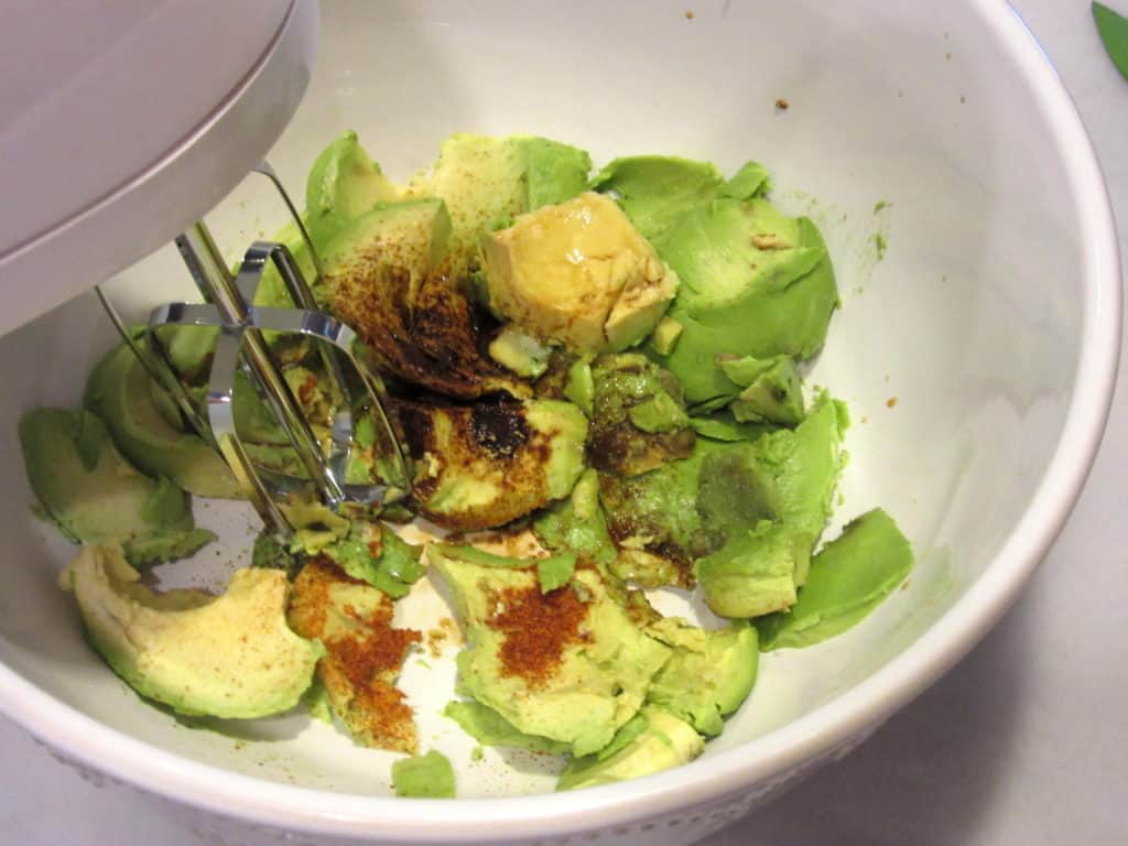 A hand mixer mashing avocados.