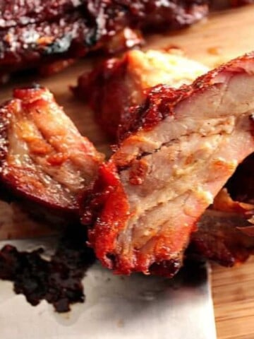 A horizontal photo of slow roasted baby back ribs on a wooden cutting board with a cleaver on the side.