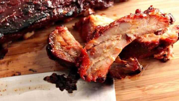 A horizontal photo of slow roasted baby back ribs on a wooden cutting board with a cleaver on the side.
