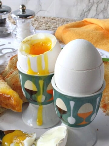 Two Air Fryer Soft Boiled Eggs in egg cups with toast on the side.