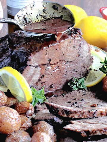 A Braised Greek Leg of Lamb with potatoes, lemons and fresh oregano on a platter.