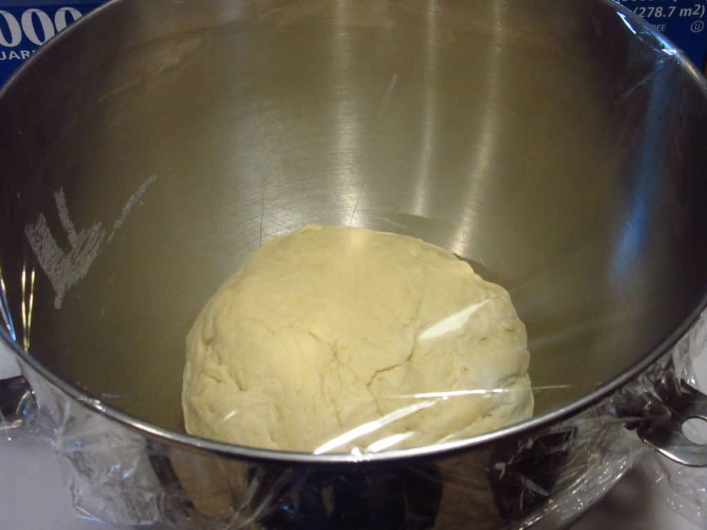 Dough in a mixing bowl covered with plastic wrap.