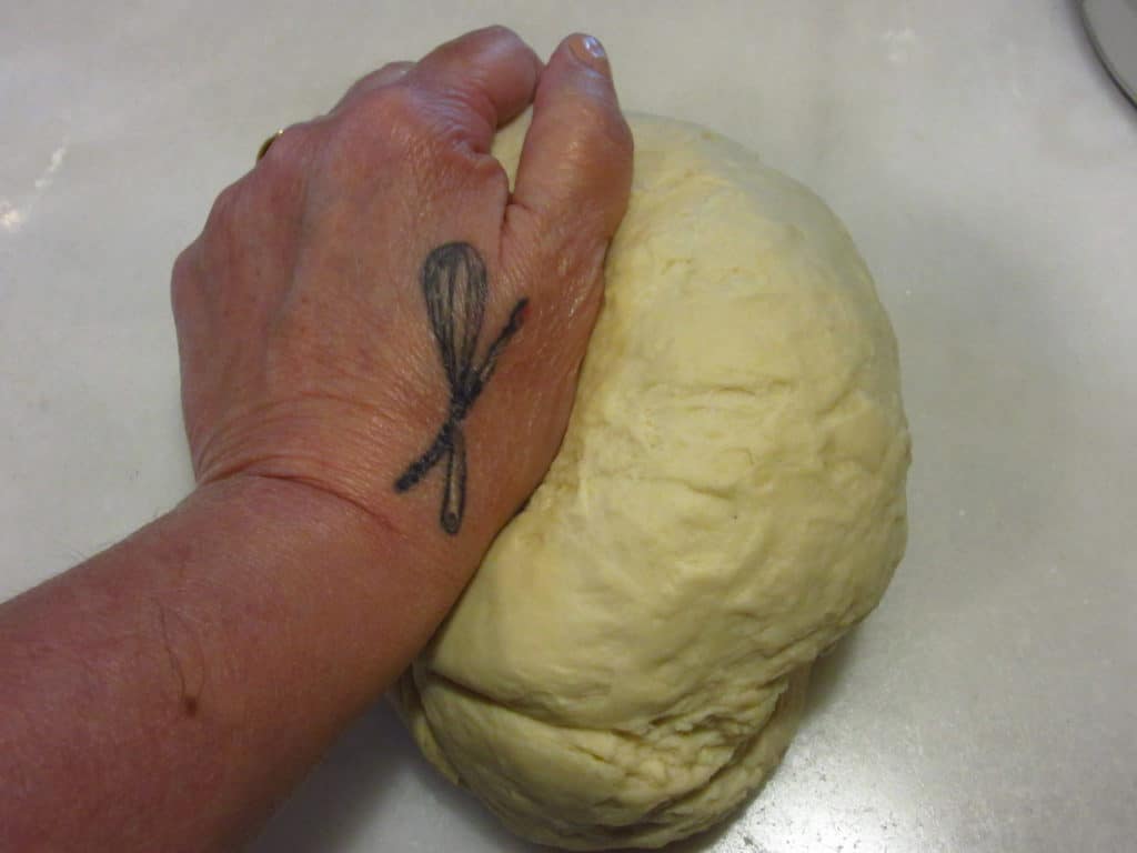 A hand with a tattoo kneading dough.