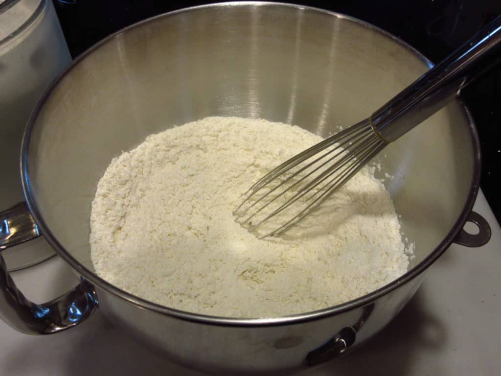 A whisk in a bowl with flour.