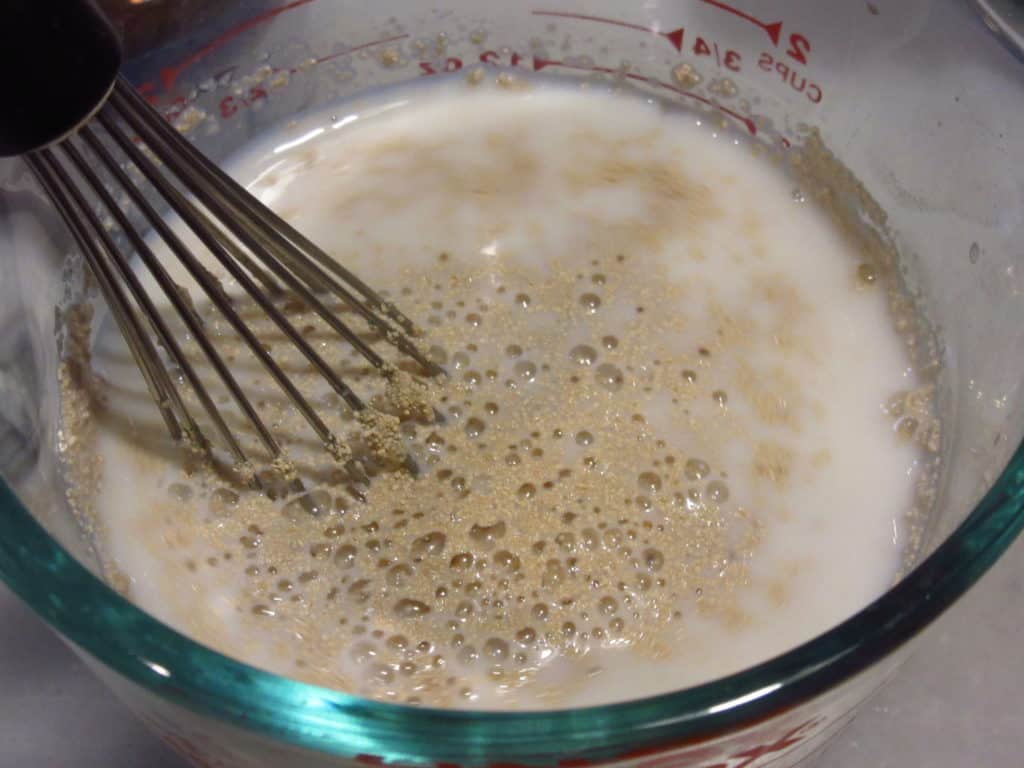 A whisk in a foamy bowl of yeast.
