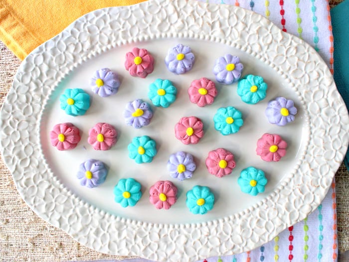 A horizontal overhead photo of a decorative oval platter filled with colorful butter mint candy flowers in pink, purple, and aqua.