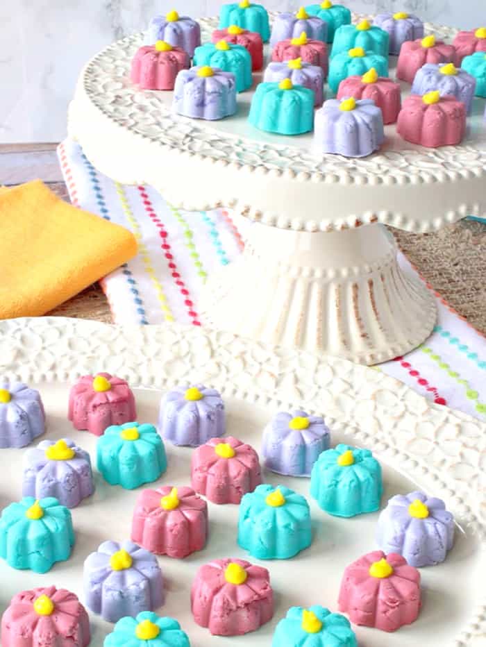 A vertical closeup image of pretty butter mint flowers on a decorative plate and cake stand.