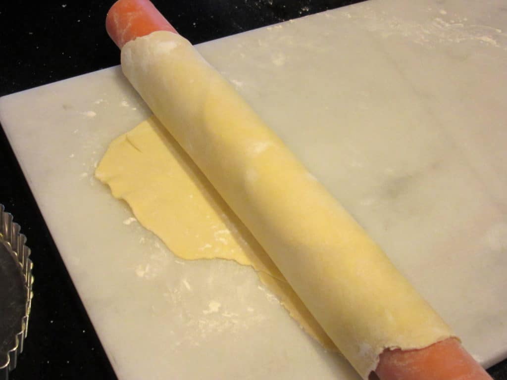 A tart dough being wound up on a rolling pin.
