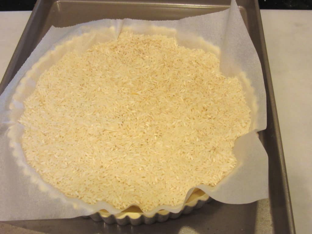 Uncooled rice on parchment paper in an unbaked tart pan with dough.