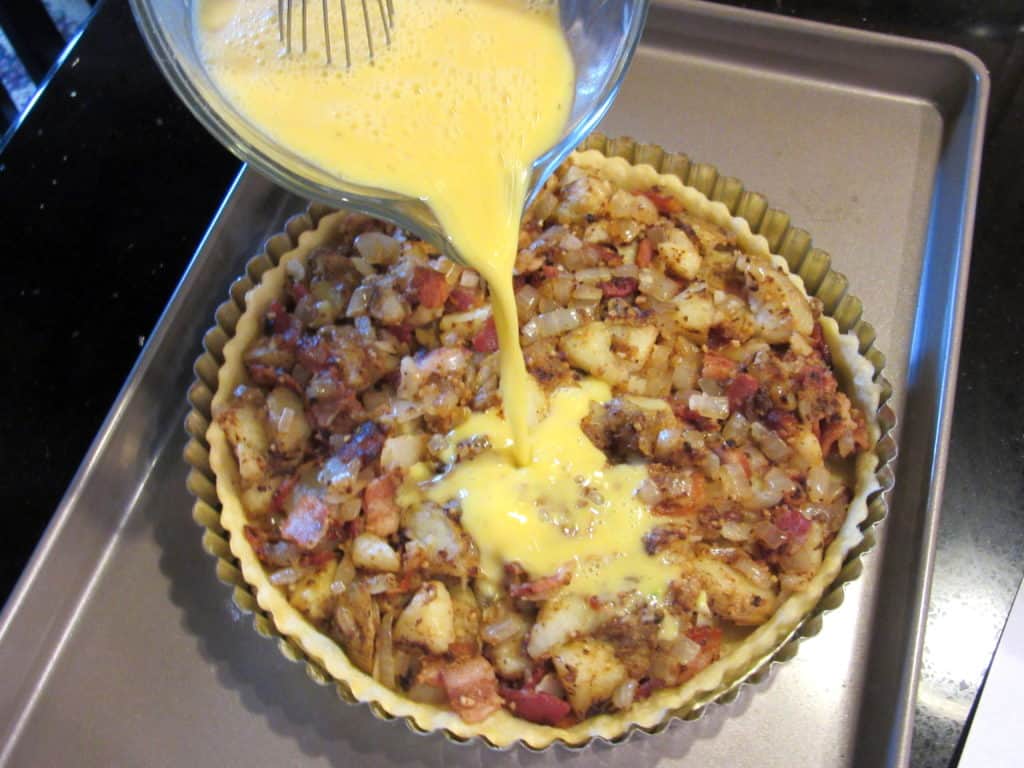 The egg mixture being poured over the potato and bacon filling for an Irish tart before baking.