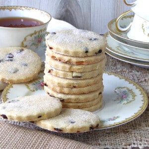 A stack of Orange Cardamom Biscuits on a pretty plate with a cup of tea in the background.