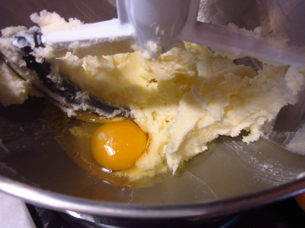 An egg in a stand mixer bowl with creamed butter.
