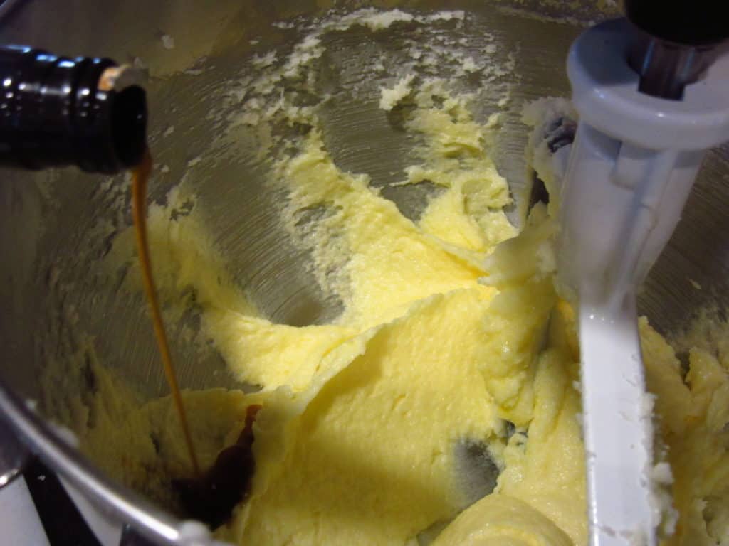 Vanilla extract being added to butter in a stand mixer bowl.