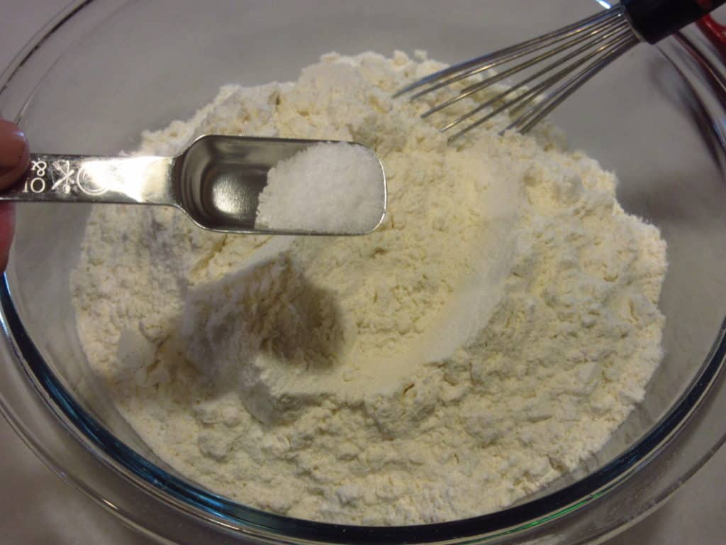 Salt being added to flour in a glass bowl.