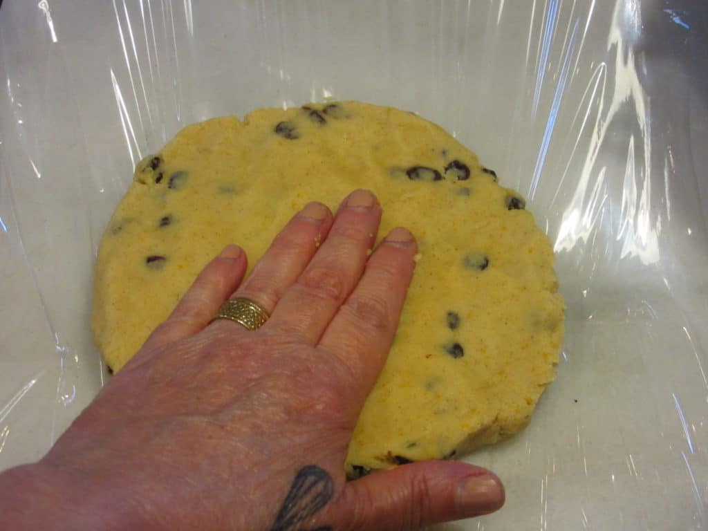 A hand flattening a disc of currant cookie dough.