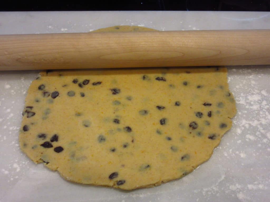 Currant cookies dough being rolled with a rolling pin.