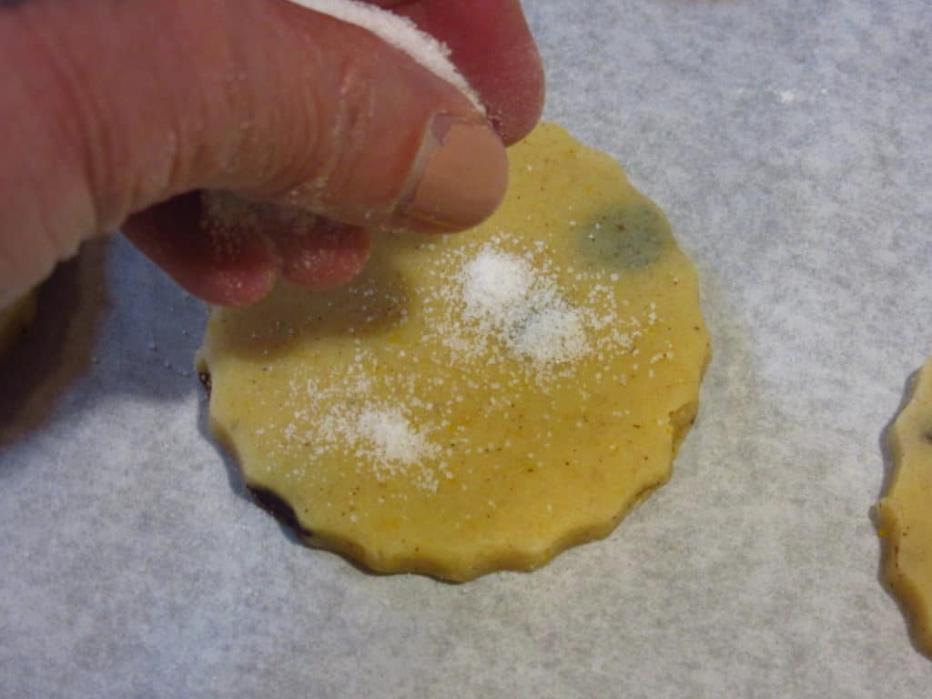Sprinkling castor sugar on a cookie before baking.