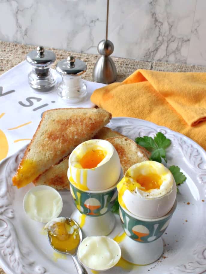 Two soft boiled eggs cooked in an air fryer on a white plate with toast and parsley.