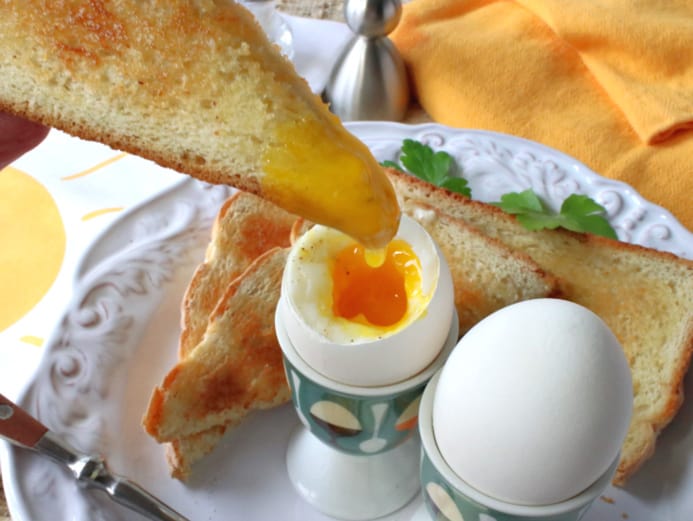 A toast point being dipped into a runny yolk of a soft boiled eggs.