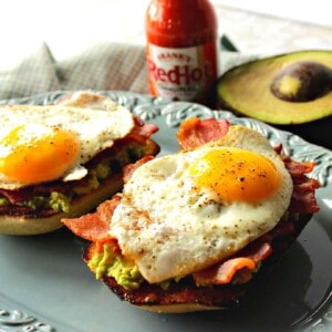 Avocado Toast with Bacon and Egg on a blue plate with hot sauce in the background.