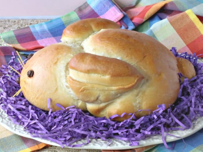 A shaped loaf of German bunny bread on a platter with purple Easter grass.