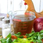 A glass measuring cup filled with Homemade Chicken Stock with veggies in the foreground.