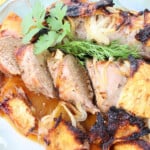 Slices of Pineapple Pork Tenderloin on a platter with pineapple, onions, and cilantro.