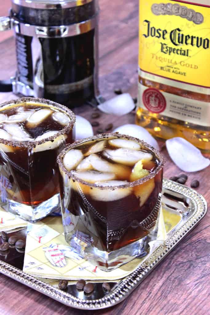 Two iced coffee margaritas on a sliver platter with ice cubes and coffee beans on the table.