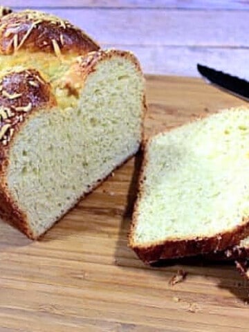 A half sliced loaf of Italian Easter Cheese Bread on a wooden board.