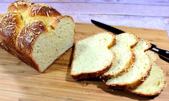 A sliced loaf of Italian cheese bread on a bread board with a serrated knife.