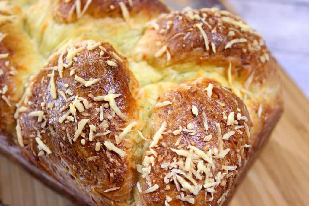 Closeup horizontal photo of a golden loaf of Italian Easter cheese bread with sprinkled shredded cheese.